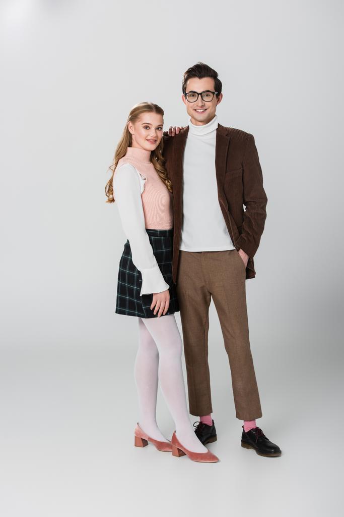 Ansicht des jungen Paares im Retro-Outfit, das auf grauem Hintergrund posiert - Foto, Bild