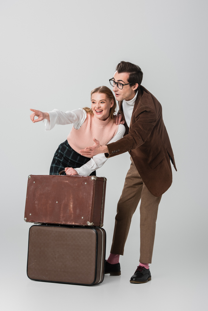 изумленная пара смотрит в сторону винтажных чемоданов на сером фоне - Фото, изображение