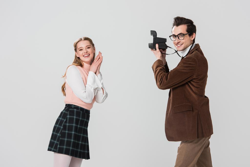 glückliche Frau in Retro-Klamotten posiert neben Mann mit Vintage-Kamera isoliert auf grau - Foto, Bild