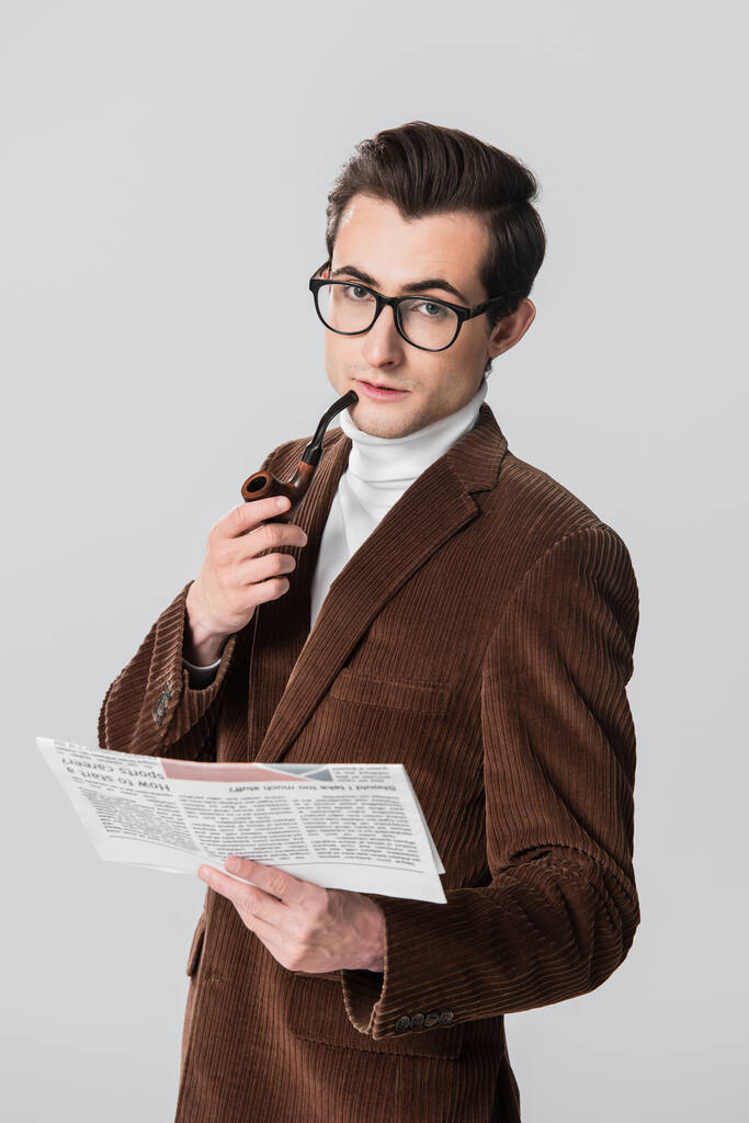 jonge man in fluwelen blazer houden roken pijp en krant geïsoleerd op grijs - Foto, afbeelding