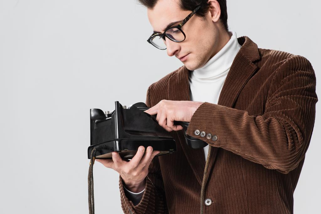 молодой человек в очках набирает номер на винтажном телефоне, изолированном на сером - Фото, изображение