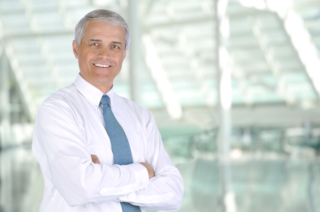 Homme d'affaires d'âge moyen souriant debout dans le hall d'un immeuble de bureaux moderne. L'homme porte une chemise blanche et une cravate avec les bras croisés. Forme horizontale
 - Photo, image