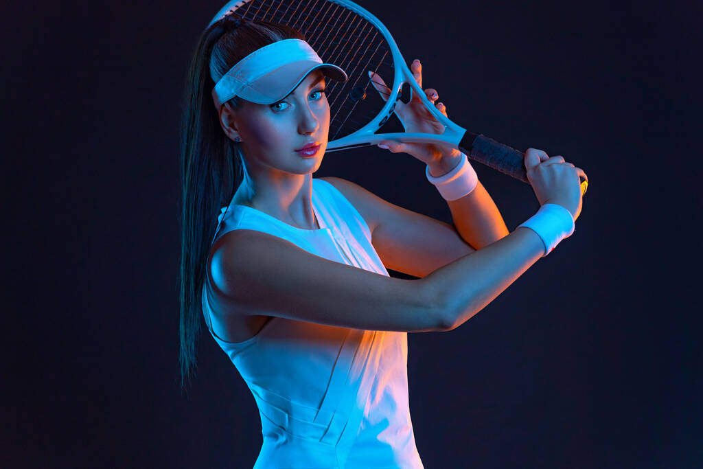 Tennispelaaja, jolla on maila valkoisessa asussa. Nainen urheilija pelaa eristetty musta tausta. - Valokuva, kuva