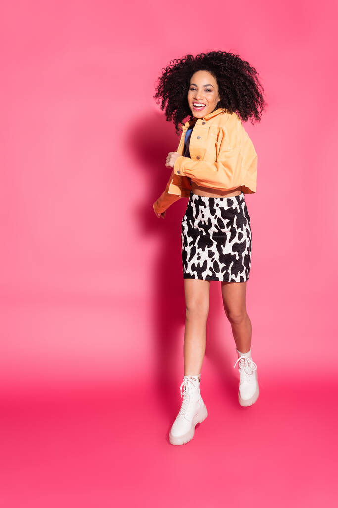 full length of african american woman in crop top, jacket and skirt with animal print running on pink - Photo, Image