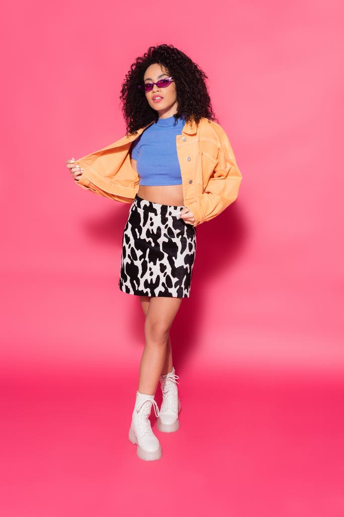 piena lunghezza della donna afroamericana alla moda in occhiali da sole in posa su rosa  - Foto, immagini