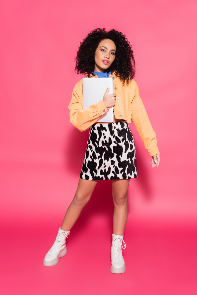full length of curly african american woman posing with laptop on pink  - Photo, Image