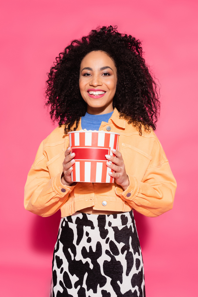 allegra donna afroamericana che tiene secchio con popcorn rosa - Foto, immagini