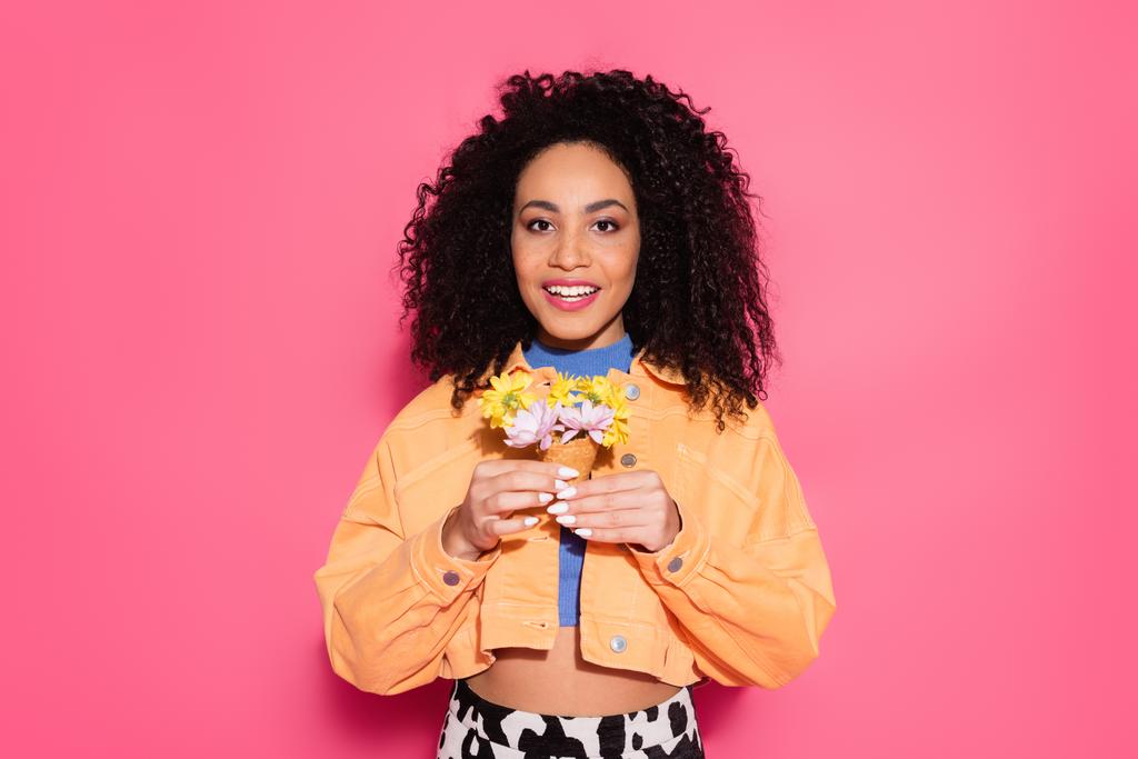 happy african american woman holding waffle cone with flowers on pink  - Photo, Image