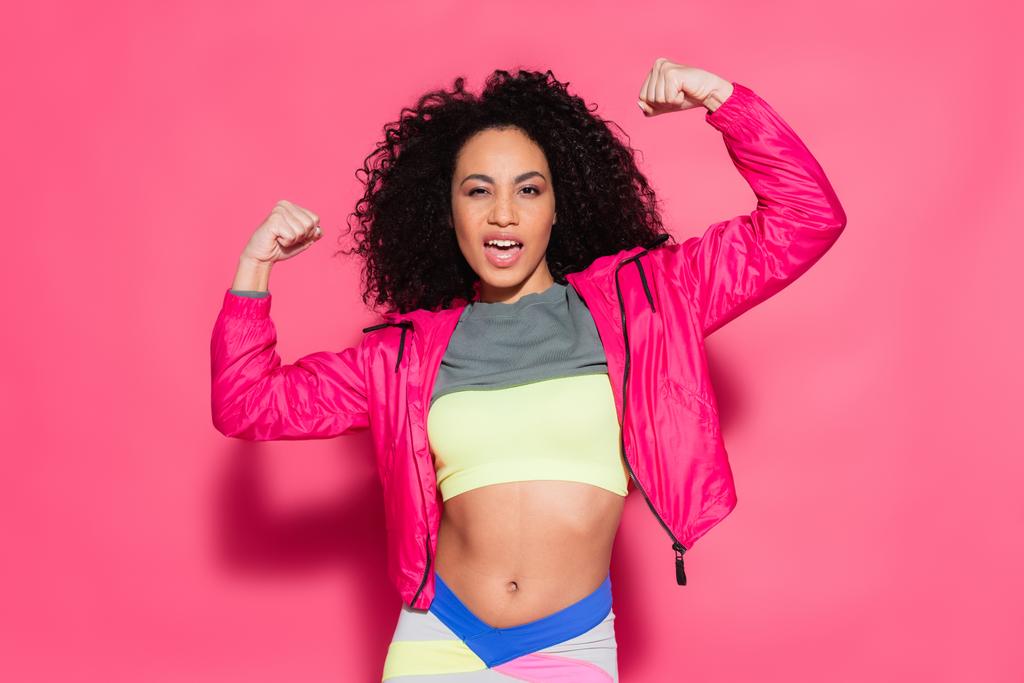 sporty brunette african american woman showing muscles while posing on pink - Photo, Image