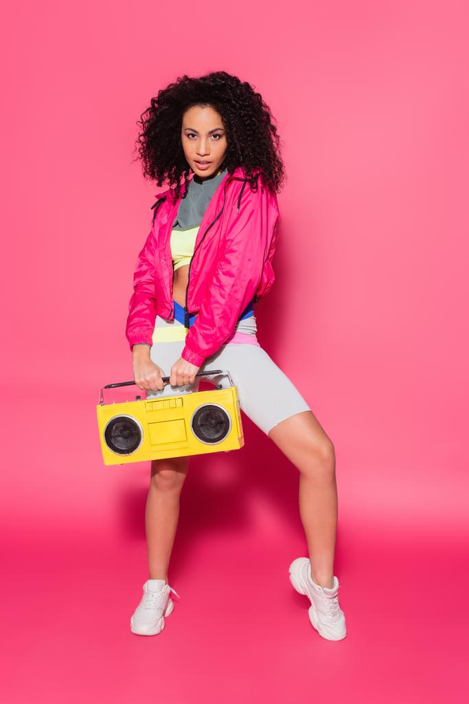 full length of sporty african american woman holding boombox on pink - Photo, Image