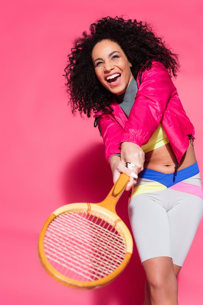здивована афроамериканська жінка тримає ракетку і грає в теніс на рожевому
 - Фото, зображення