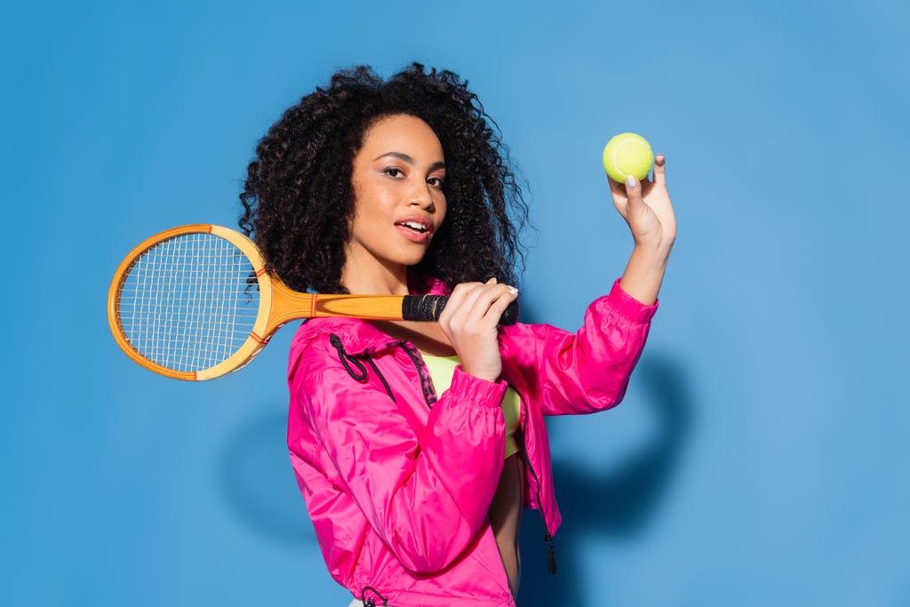 σγουρή Αφροαμερικανή που κρατάει ρακέτα και μπάλα του τένις στο μπλε - Φωτογραφία, εικόνα