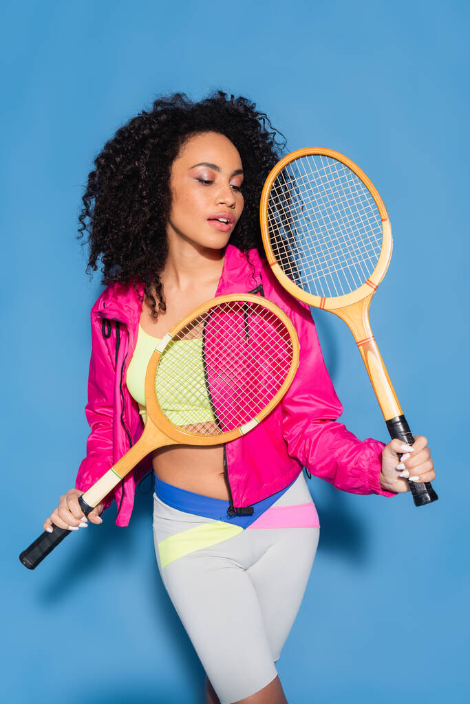 jong afrikaans amerikaans vrouw holding tennis rackets op blauw - Foto, afbeelding