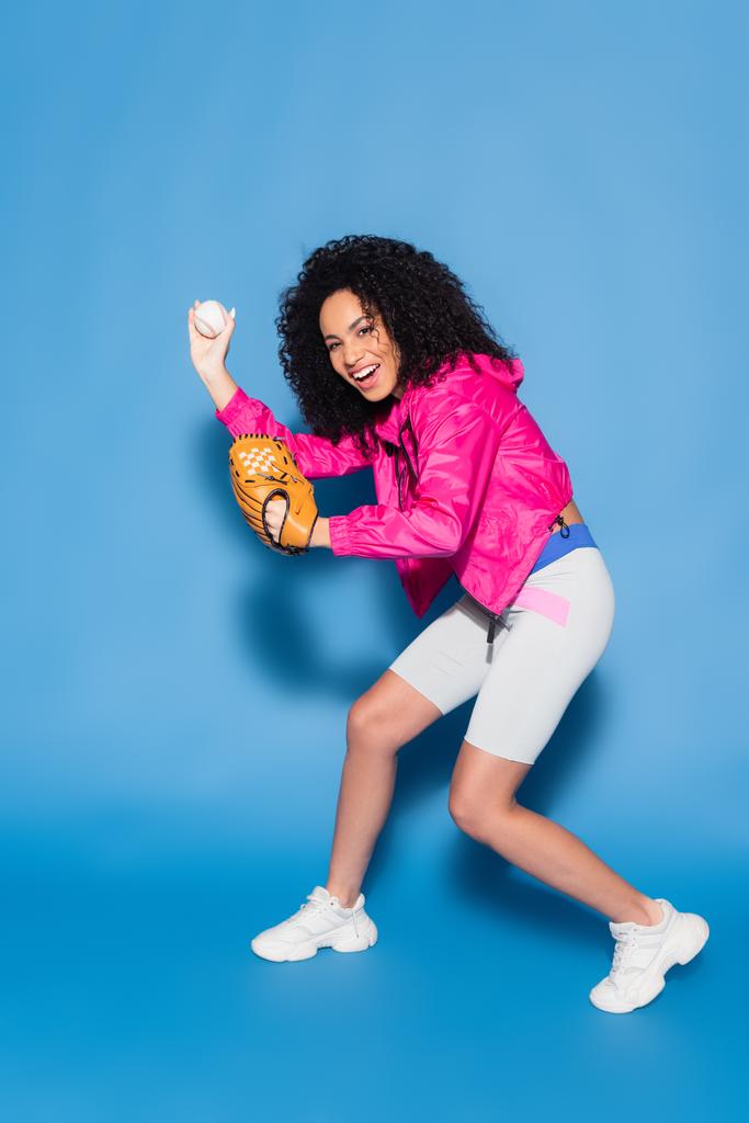 longitud completa de la mujer afroamericana emocionada jugando béisbol en azul - Foto, Imagen