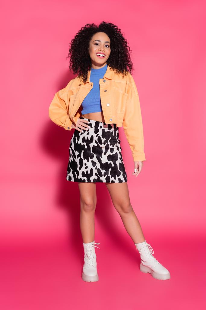 full length of happy african american woman in skirt with animal print, jacket and crop top posing on pink  - Photo, Image
