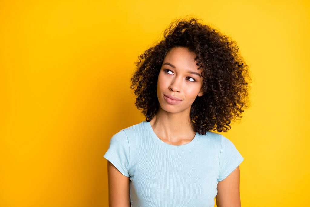 Фотопортрет цікавої афро-американської жінки, яка дивиться на порожній простір ізольований на яскраво-жовтому тлі - Фото, зображення