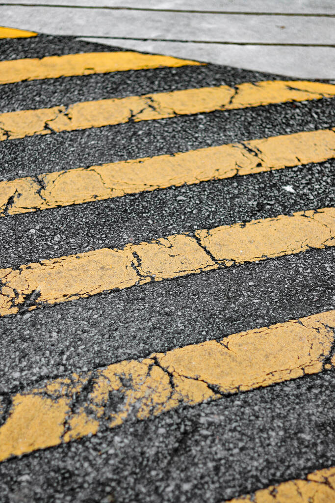 Крупный план выветрившихся и старых диагональных желтых линий на асфальтированной дороге - Фото, изображение
