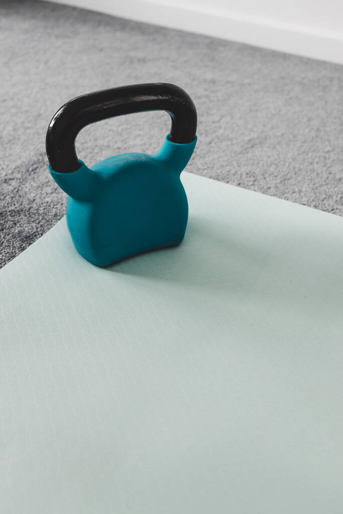 gimnasio en casa con artículos de fitness mixtos que incluyen esterilla de yoga y kettlebell con sutiles tonos grises y azules  - Foto, imagen