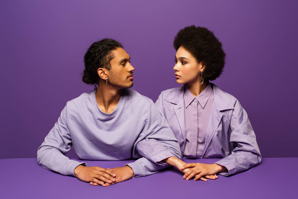 hombre afroamericano y mujer joven rizada mirándose aislados en púrpura  - Foto, Imagen