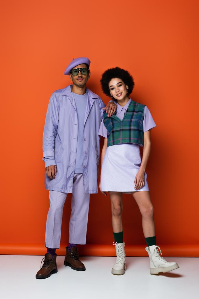piena lunghezza di trendy afro-americano uomo e donna sorridente mentre posa su arancione  - Foto, immagini