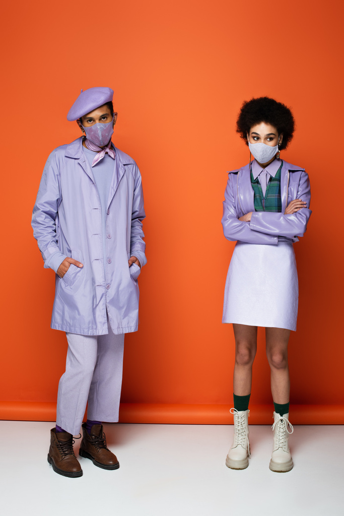 longitud completa de la pareja afroamericana de moda en máscaras protectoras de pie en naranja  - Foto, imagen