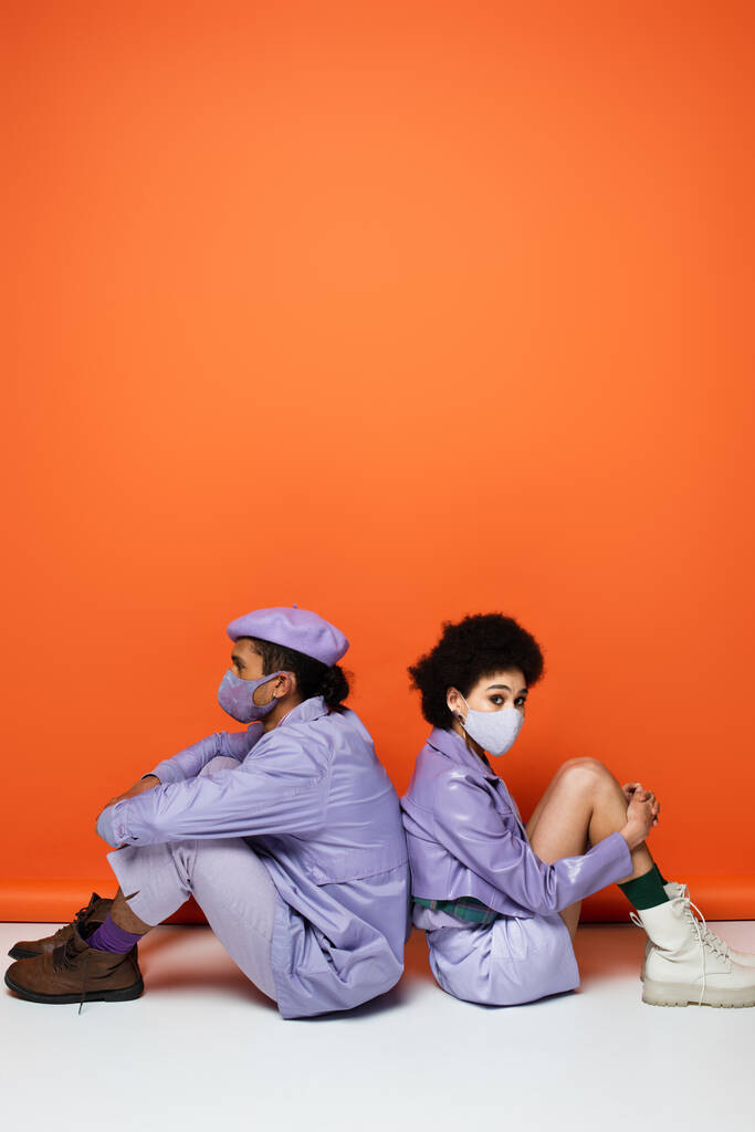 comprimento total de casal americano africano na moda em máscaras protetoras sentado em laranja  - Foto, Imagem