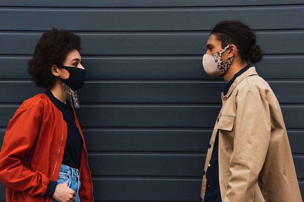 fiatal afro-amerikai nő és stílusos férfi védő maszkok nézik egymást kívül  - Fotó, kép
