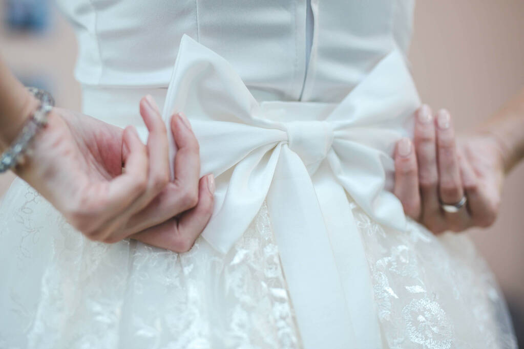 Un primer plano de la novia fijando su arco en su vestido de novia blanco - Foto, imagen