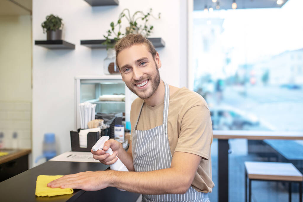Усміхнений чоловік з дезінфікуючим засобом і серветкою в кафе
 - Фото, зображення