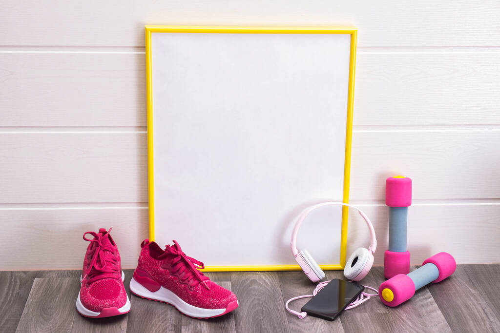 sport otthon - súlyzók és rózsaszín tornacipők, egy tábla sárga kerettel, jegyzetekhez, fejhallgatókhoz és egy mobiltelefonhoz fehér alapon - Fotó, kép