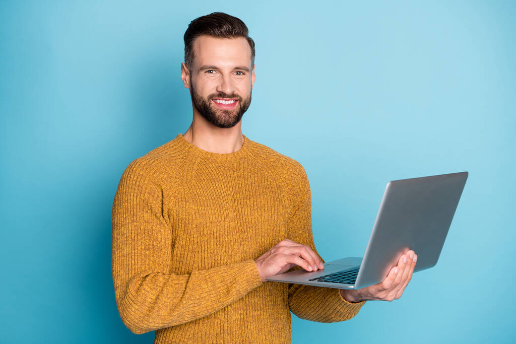 Портрет привабливого працівника веселого хлопця, який тримається в руках за допомогою ноутбука, ізольованого на яскраво-блакитному фоні
 - Фото, зображення