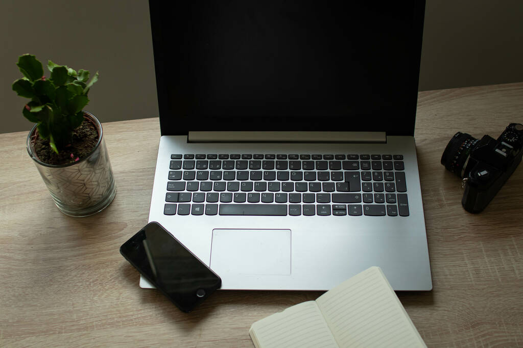 Um laptop, um caderno aberto, um celular e uma planta em uma mesa de escritório - Foto, Imagem