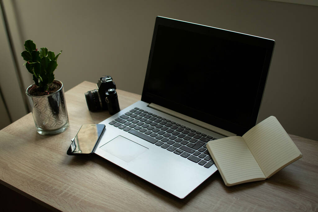 Un portátil, un cuaderno abierto, un teléfono celular y una planta en una mesa de oficina - Foto, imagen