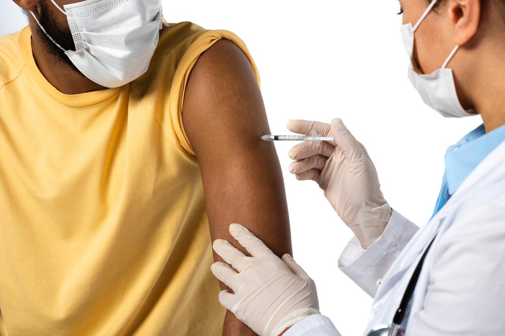Paciente afroamericano en máscara protectora cerca del médico haciendo vacunación en primer plano borroso aislado en blanco  - Foto, Imagen