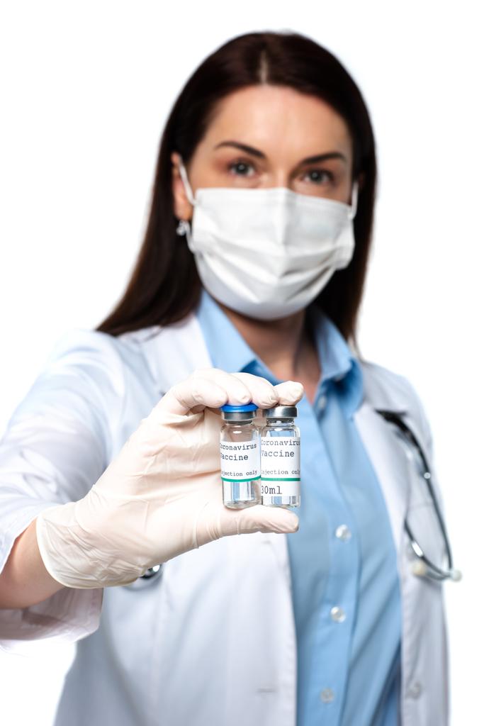 Θολή γιατρός σε ιατρική μάσκα κρατώντας βάζα με εμβόλιο που απομονώνεται σε λευκό  - Φωτογραφία, εικόνα
