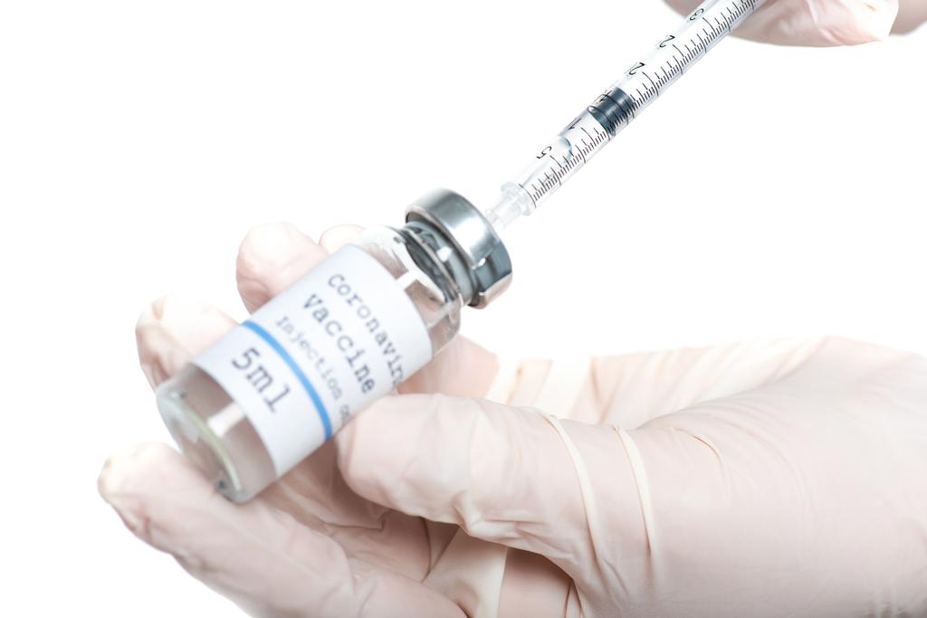 Обрезанный вид шприца и банки с коронавирусной вакциной в руках врача, изолированного на белом  - Фото, изображение