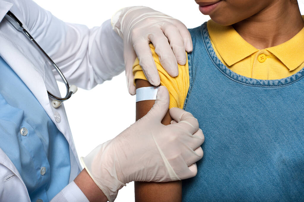 白に隔離されたアフリカ系アメリカ人患者の腕に接着石膏を適用小児科医の作物ビュー  - 写真・画像