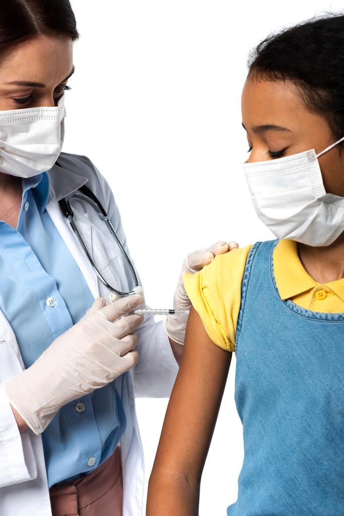 Médecin faisant une injection de vaccin à un enfant afro-américain dans un masque médical isolé sur blanc  - Photo, image