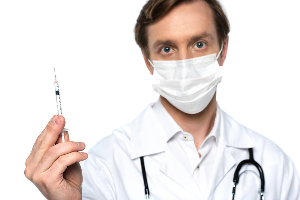 Fehérre izolált, orvosi maszkban lévő, homályos orvos kezében lévő fecskendő  - Fotó, kép