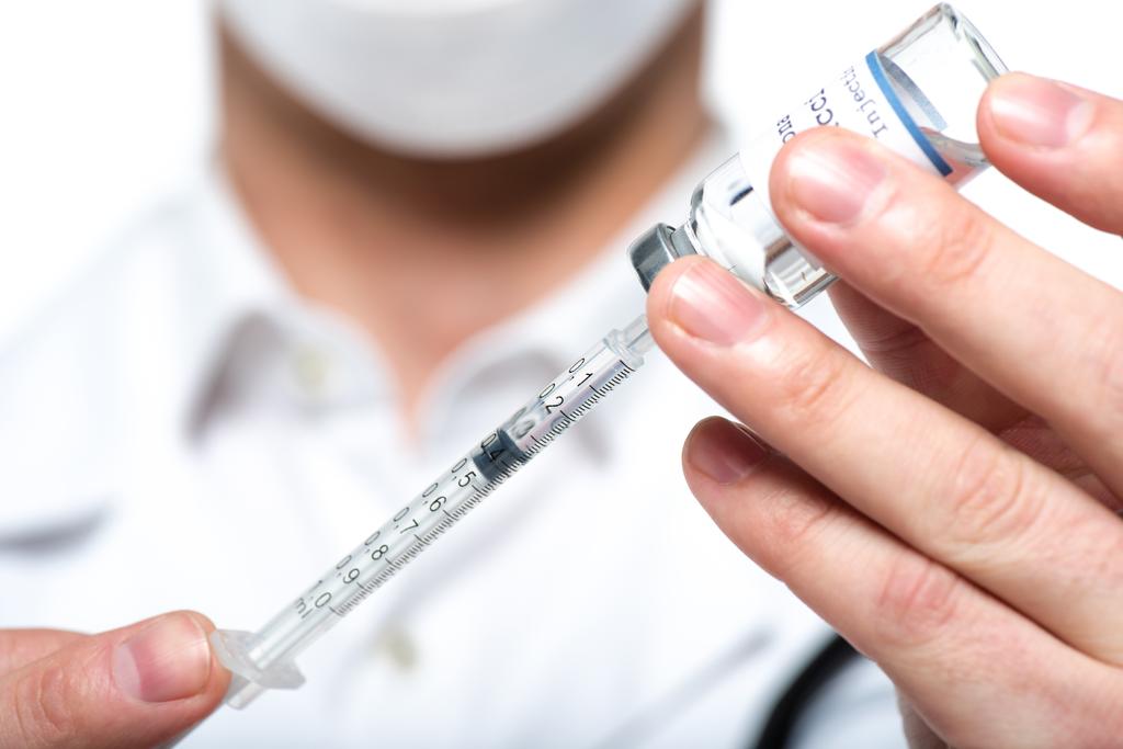Vista ravvicinata della siringa e del vaccino nelle mani del medico sfocato isolato sul bianco  - Foto, immagini