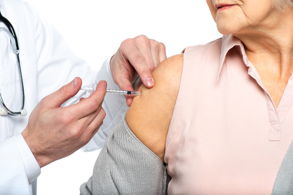 Προβολή της ηλικιωµένης γυναίκας κοντά στο γιατρό µε σύριγγα κατά τη διάρκεια εµβολιασµού που απομονώθηκε σε λευκά  - Φωτογραφία, εικόνα