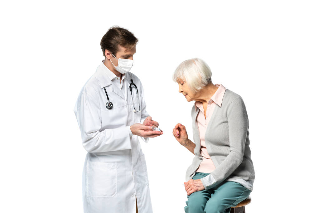 Врач в медицинской маске держит вакцину рядом с пожилым пациентом изолированы на белом  - Фото, изображение