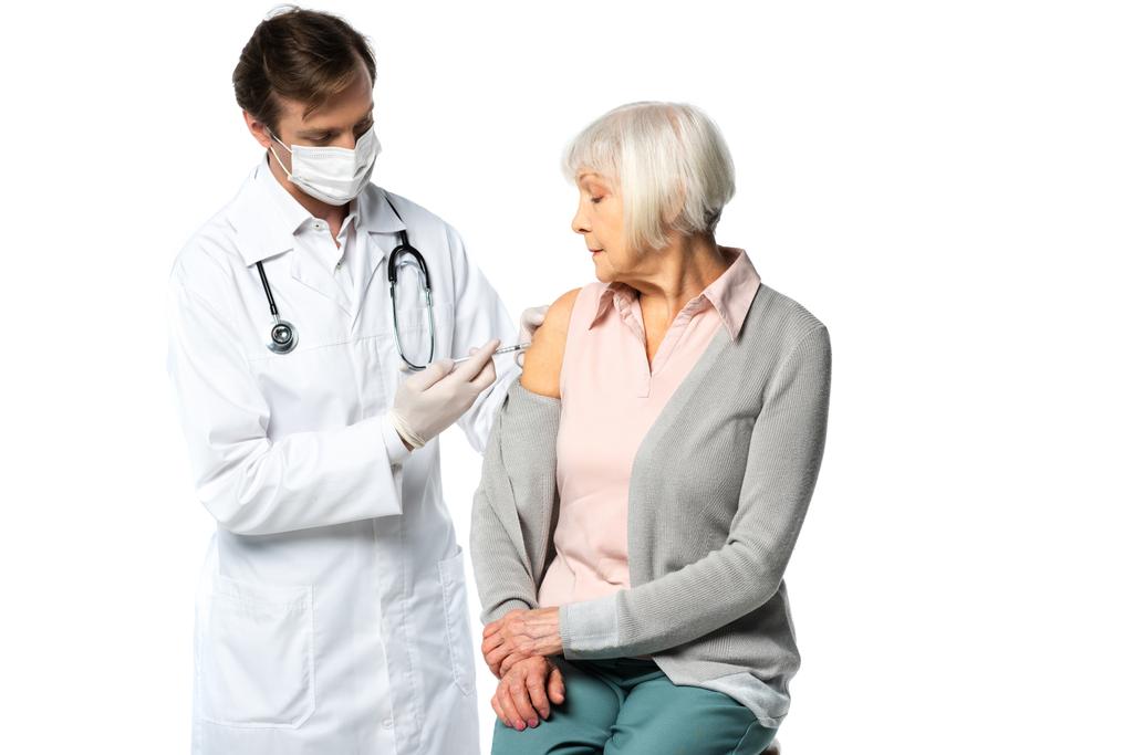 Médecin masqué faisant une injection de vaccin à un patient âgé isolé sur du blanc  - Photo, image