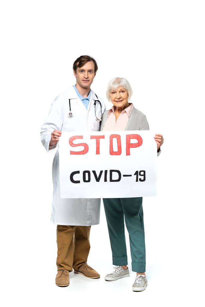 Senor ασθενή χαμογελώντας κρατώντας πλακάτ με stop covid-2019 γράμματα κοντά στο γιατρό σε λευκό φόντο  - Φωτογραφία, εικόνα
