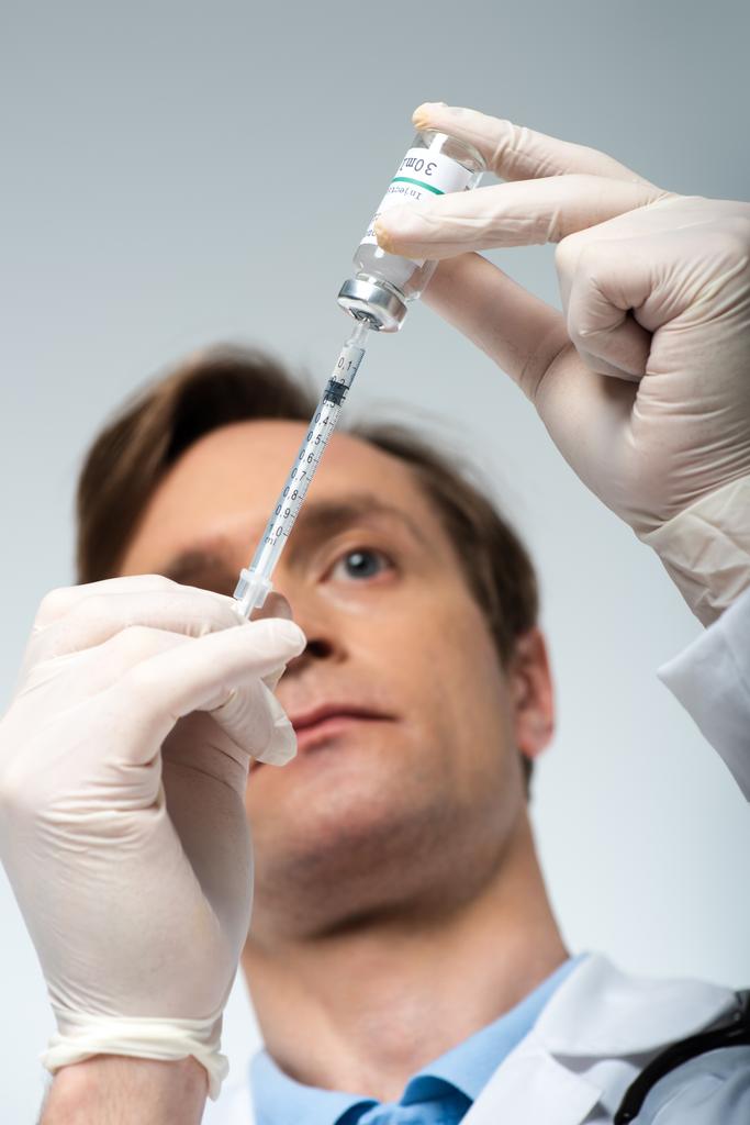 灰色で隔離されたぼやけた医師の手の中のワクチンと注射器の低角度ビュー  - 写真・画像