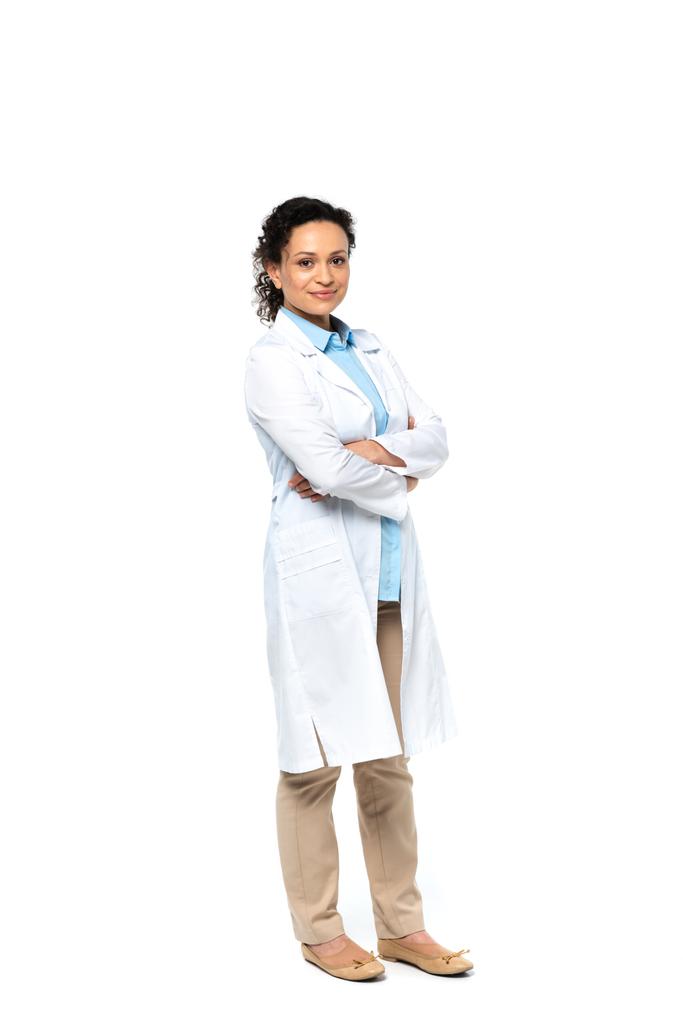 Sonriente médico afroamericano de pie con los brazos cruzados sobre fondo blanco  - Foto, Imagen