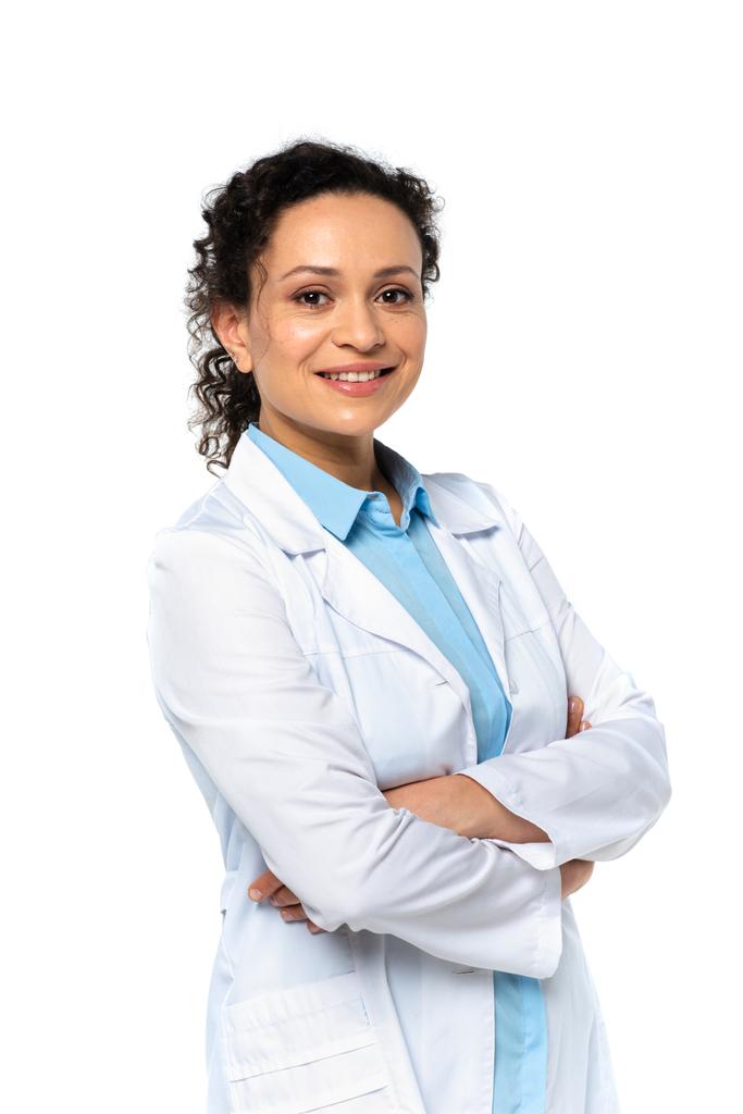 Χαμογελώντας αφροαμερικανός γιατρός με λευκό παλτό κοιτάζοντας κάμερα που απομονώνεται σε λευκό  - Φωτογραφία, εικόνα