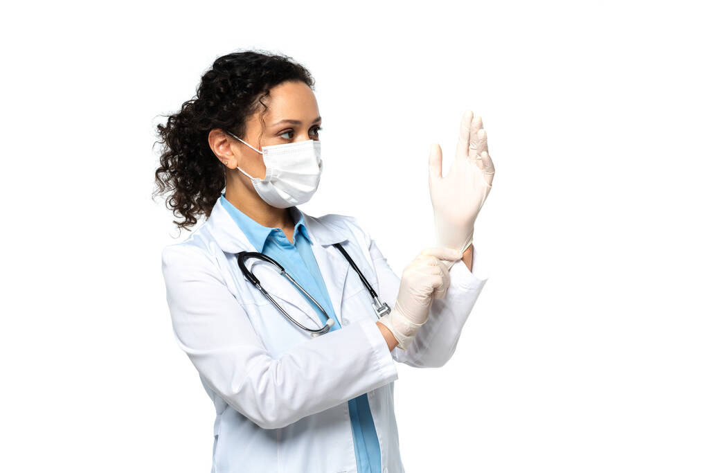 Африканский американский врач в белом халате и медицинской маске в латексных перчатках, изолированных на белом  - Фото, изображение