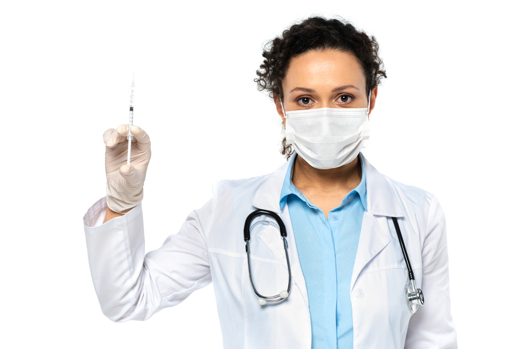 Medico afroamericano in maschera medica contenente siringa con vaccino isolato su bianco  - Foto, immagini