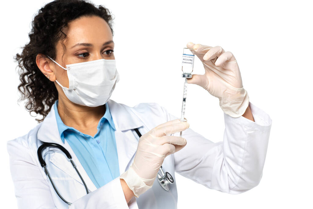 Medico afroamericano in maschera medica raccogliendo il vaccino coronavirus in siringa isolata su bianco  - Foto, immagini